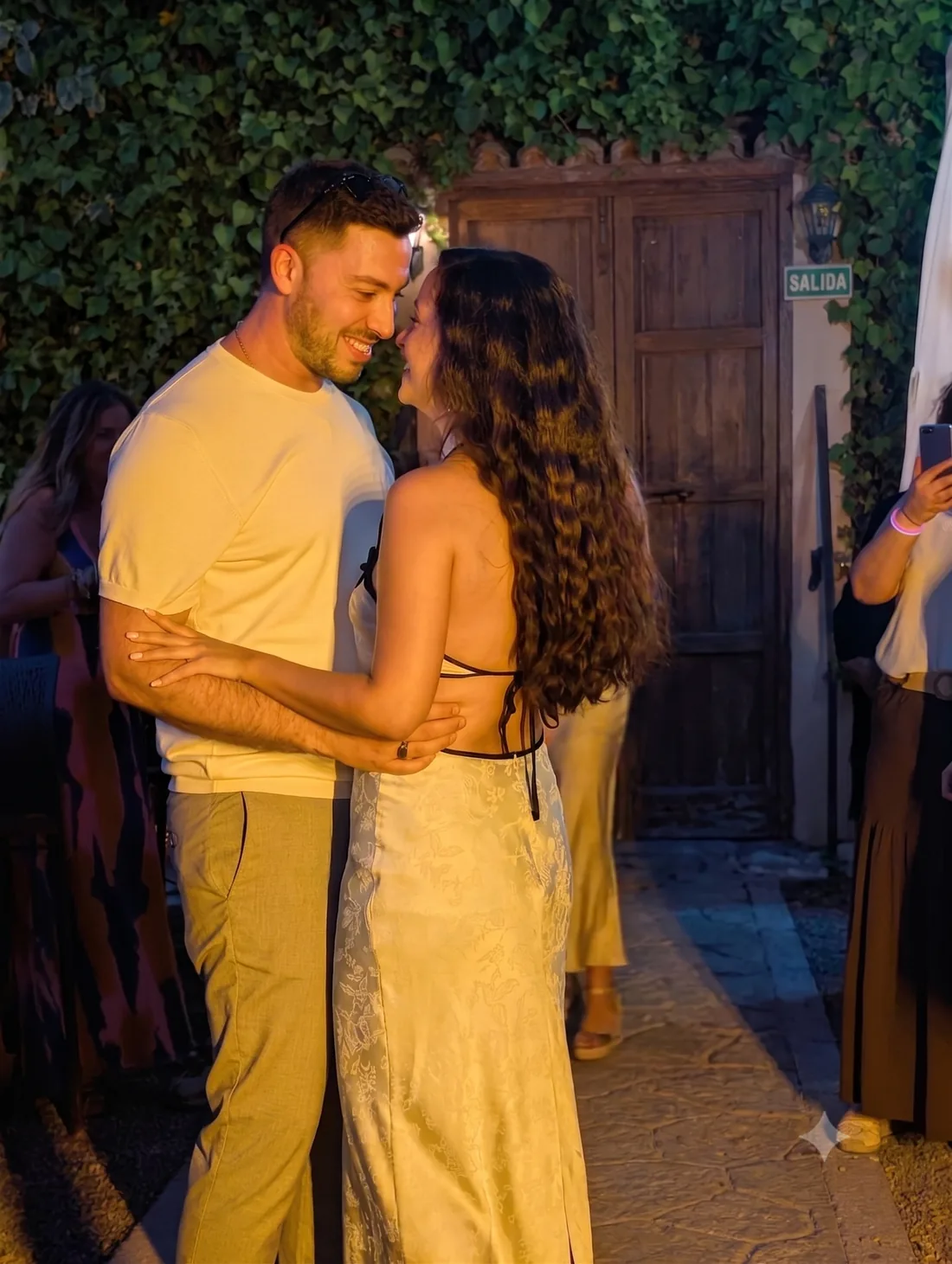 Pareja bailando abrazada en el patio de El Corral de las Cigüeñas durante una celebración, con el muro de hiedra al fondo