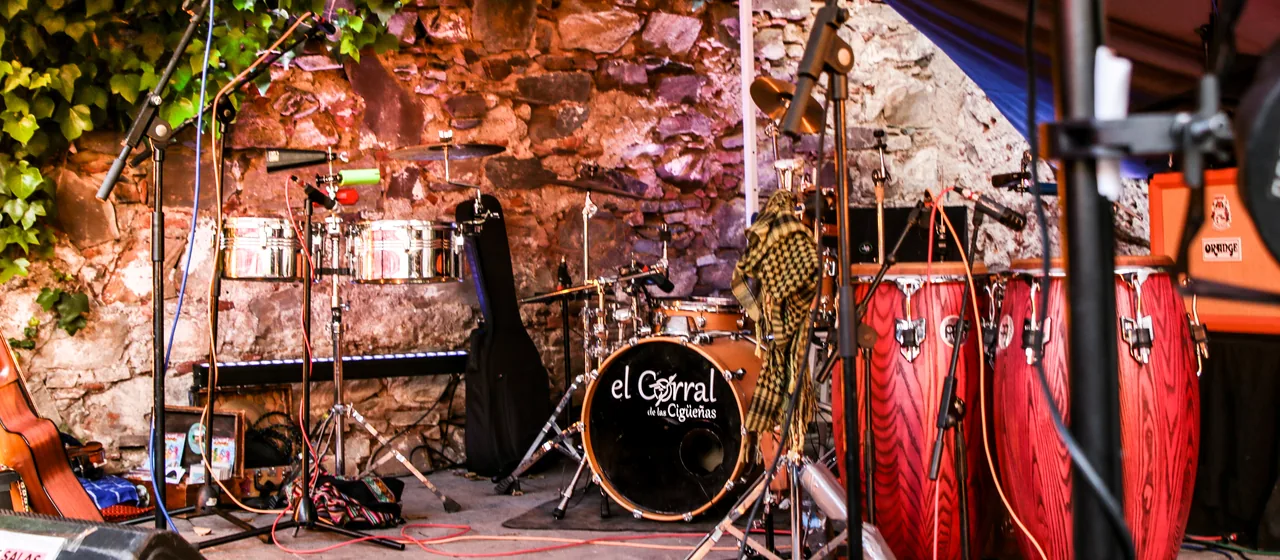 Escenario del patio de El Corral de las Cigüeñas montado antes de un concierto: batería con el logo de la casa, congas, timbales y microfonía