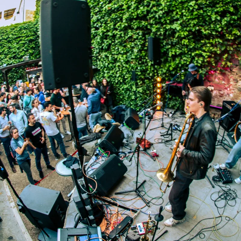Concierto de día en el patio de El Corral de las Cigüeñas: una trompetista sobre el escenario y el público sentado alrededor
