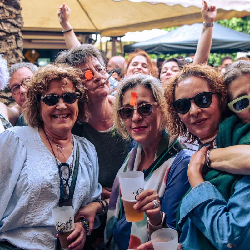 Grupo de amigas con sus consumiciones, sonriendo entre el público de un concierto en El Corral de las Cigüeñas