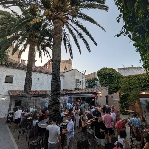 Atardecer en el patio de El Corral de las Cigüeñas, con las palmeras, las mesas altas y la gente de pie