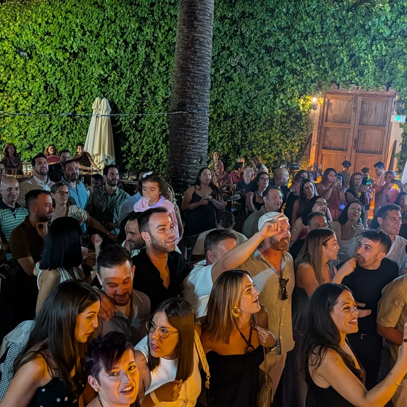 Patio de El Corral de las Cigüeñas lleno de gente de noche, junto al muro de hiedra y el portón de madera