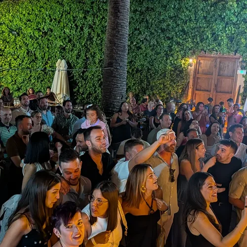 Patio de El Corral de las Cigüeñas lleno de gente de noche, junto al muro de hiedra y el portón de madera