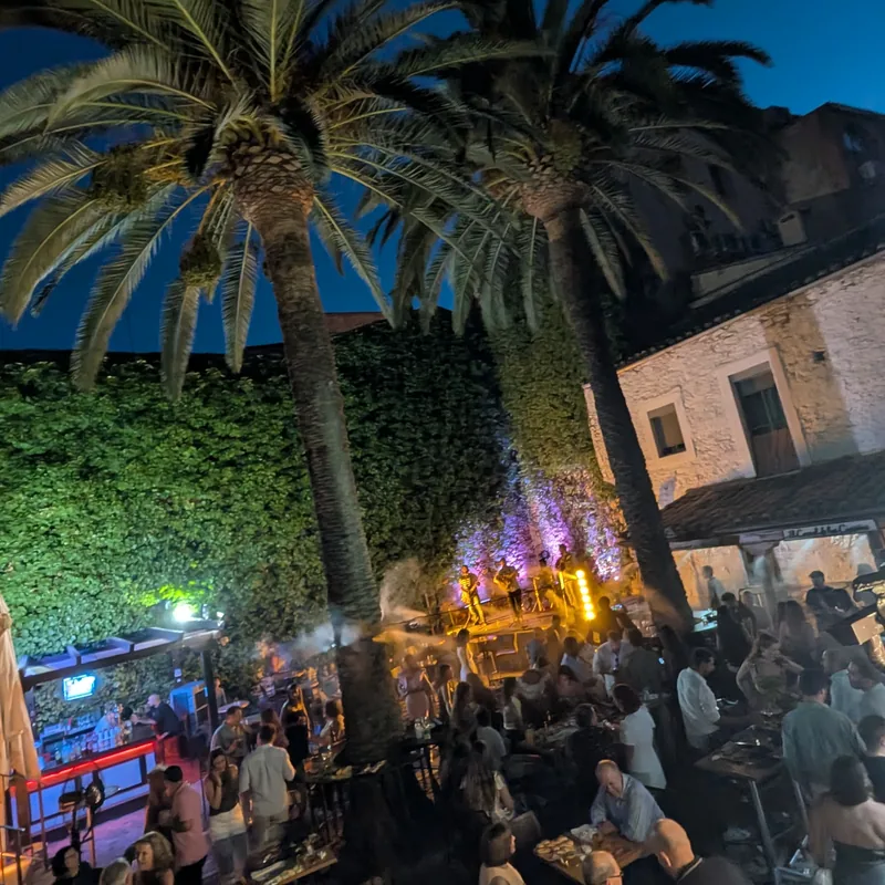 Vista del patio de El Corral de las Cigüeñas de noche, con las palmeras recortadas contra el cielo y el escenario al fondo