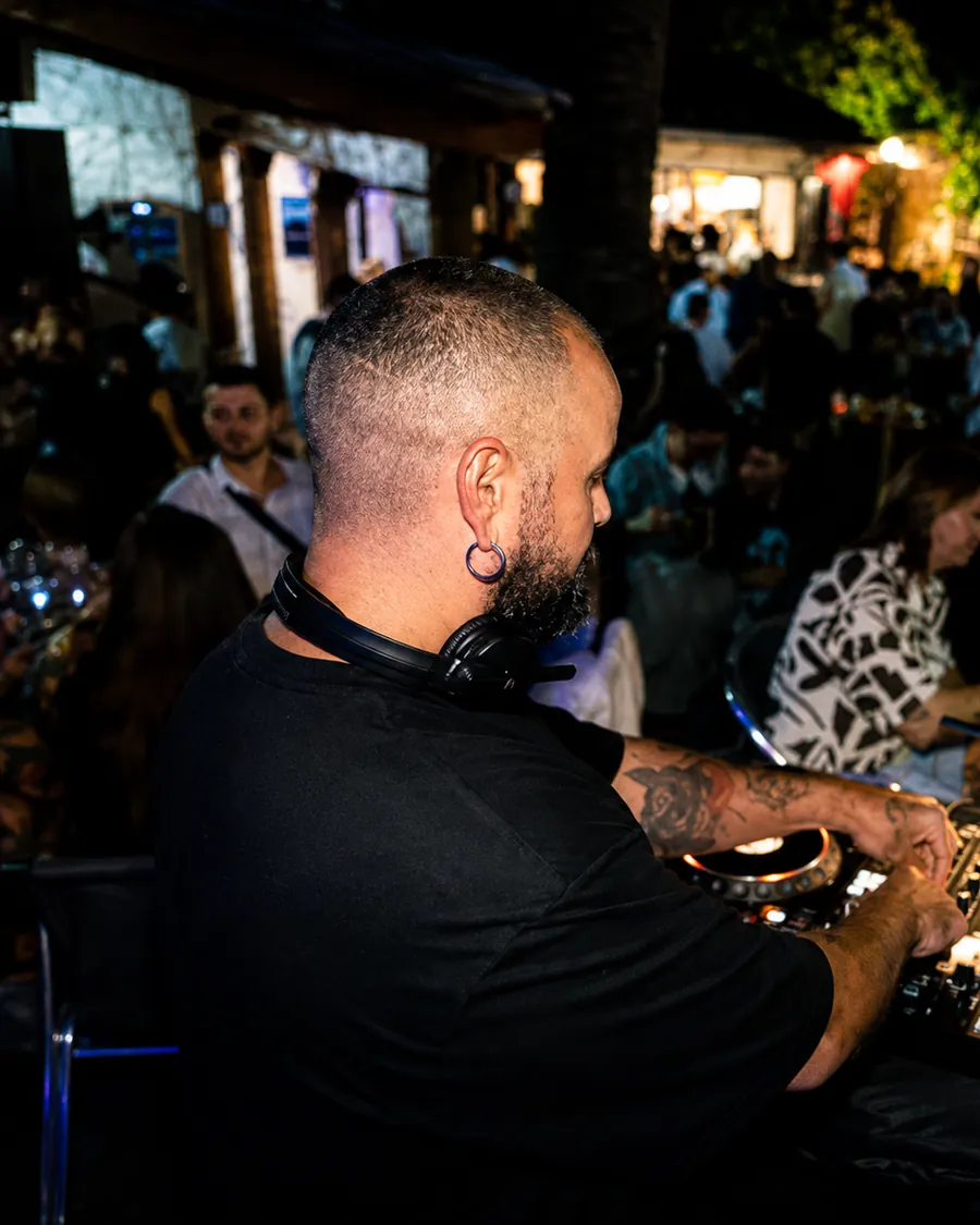 El DJ de espaldas ante los platos en el patio de noche, con el público al fondo
