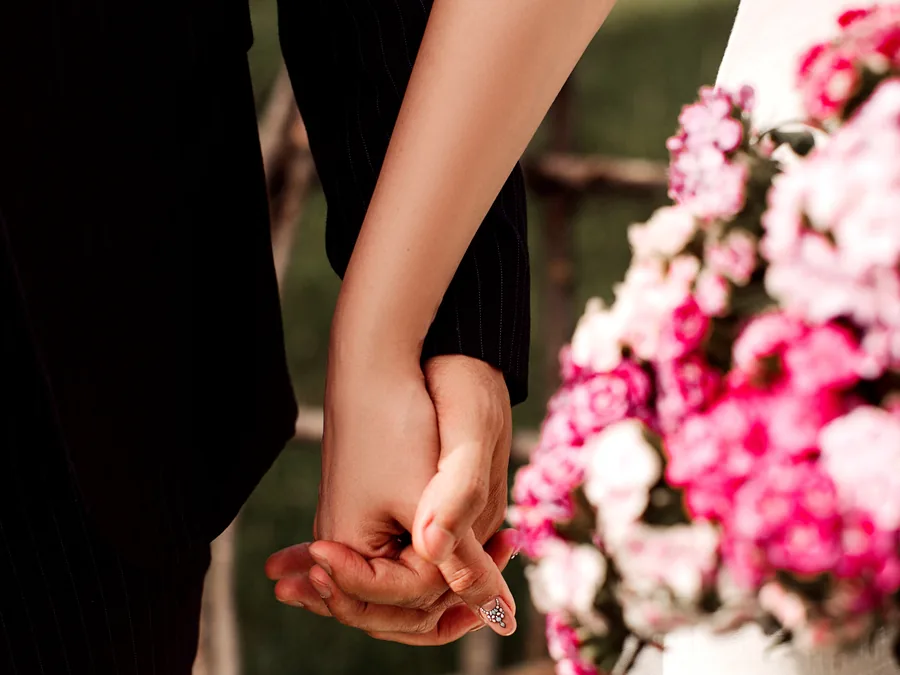 Manos entrelazadas de una pareja junto a un ramo de flores, antes de su boda