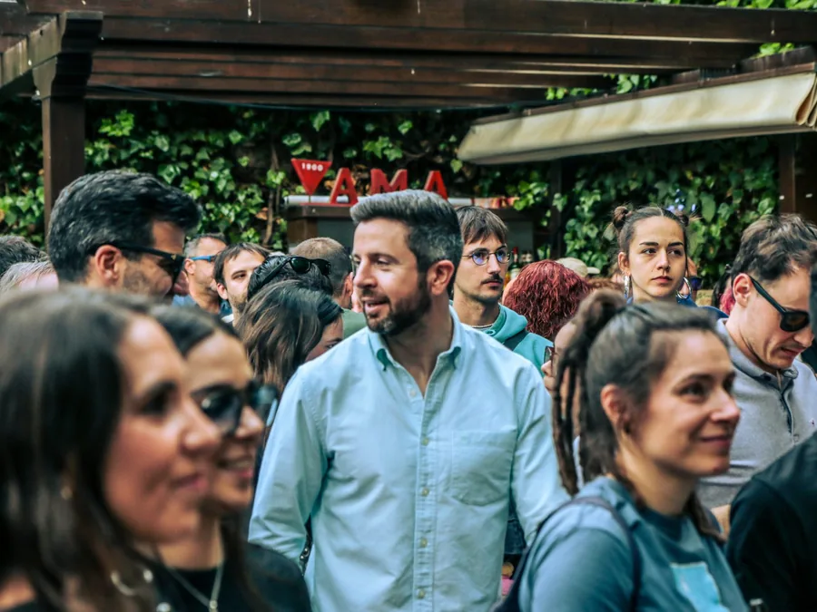 Grupo numeroso de gente charlando en el patio de El Corral de las Cigüeñas, junto a la barra y el muro de hiedra