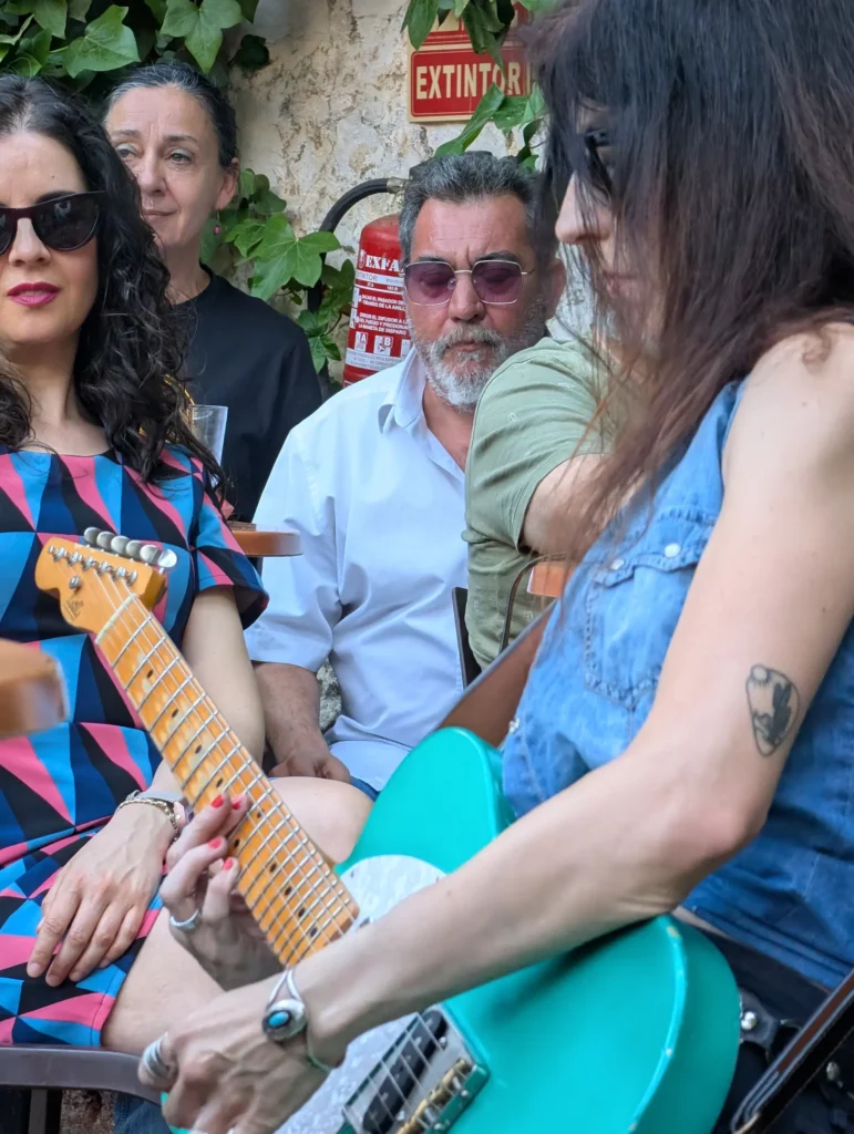 Una guitarrista toca su Telecaster turquesa a un palmo del público, sentado alrededor